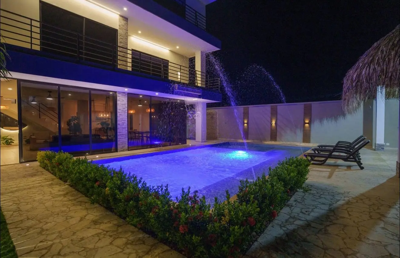 Piscina iluminada de noche frente a la fachada de tres pisos