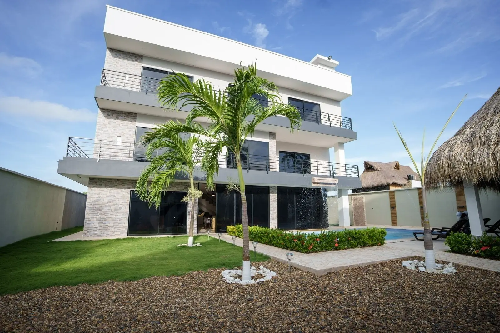 Fachada de la casa hotel con jardín, palmeras y kiosco de palma